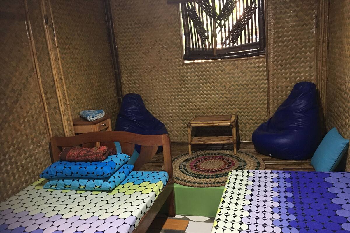 Ein Zimmer mit einem Bett, zwei Sitzsäcken, einem kleinen Holztisch und einem Fenster mit Bambusrollos.