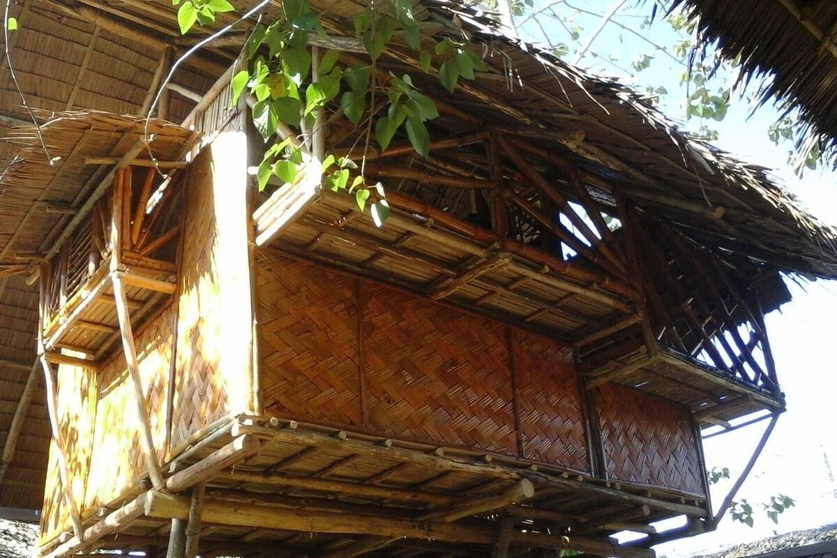 Ein traditionelles Holzhaus mit einem Reetdach, einem Balkon und einer gewebten Bambuskonstruktion.