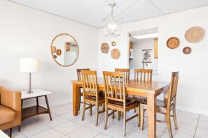 A dining area with a wooden table and chairs, a round mirror, and wall decor. - Bright & Modern Penthouse w/ Stunning Ocean Views, Heated Pool & BBQ Grills! (Cocoa Beach)