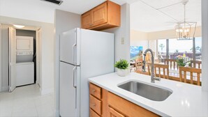 A modern kitchen with white appliances, wooden cabinets, and a large window overlooking a patio area. - Bright & Modern Penthouse w/ Stunning Ocean Views, Heated Pool & BBQ Grills! (Cocoa Beach)
