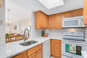 A modern kitchen with wooden cabinets, a white countertop, a stainless steel sink, a microwave, and an oven. - Bright & Modern Penthouse w/ Stunning Ocean Views, Heated Pool & BBQ Grills! (Cocoa Beach)