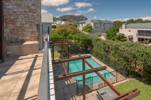 A rooftop pool with a wooden deck and a view of surrounding buildings and mountains.
