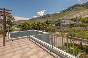 A rooftop terrace with a view of a mountainous landscape, a pergola, and a swimming pool.