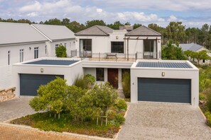 A modern two-story house with a garage, a balcony, and a landscaped garden.