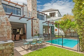 Una casa moderna con fachada de piedra, piscina y zona de patio cubierta.