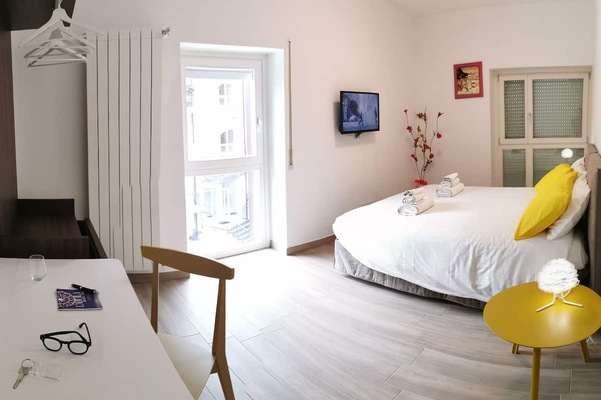 A modern bedroom with a bed, a desk, a chair, a small table, and a window.