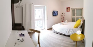 A modern bedroom with a bed, a desk, a chair, a small table, and a window.