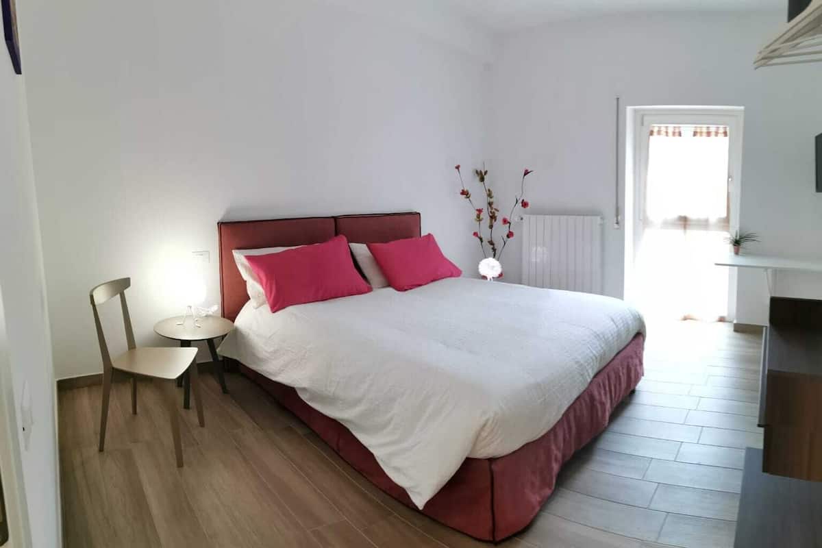 A bedroom with a bed, a chair, a small table, and a radiator.