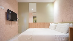 A neatly made bed with white linens, a mounted flat-screen TV on the wall, and a wooden headboard.