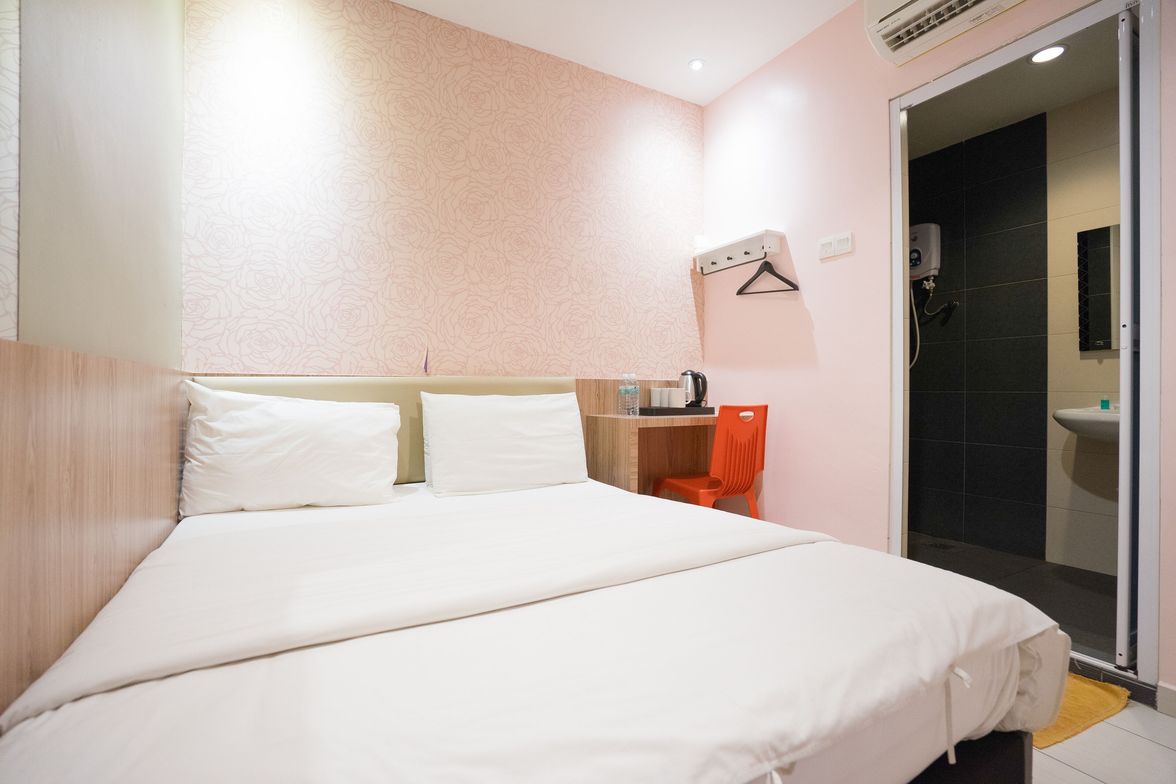 A hotel room with a large bed, a desk with a chair, a shower area, and a sink.