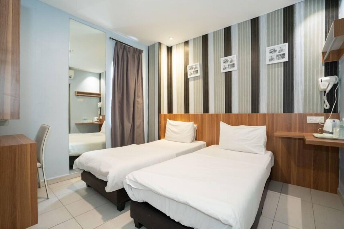 A hotel room with two beds, a desk, a chair, a mirror, and a striped wall.