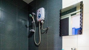 A bathroom with dark tiled walls, a white sink, and a handheld showerhead.