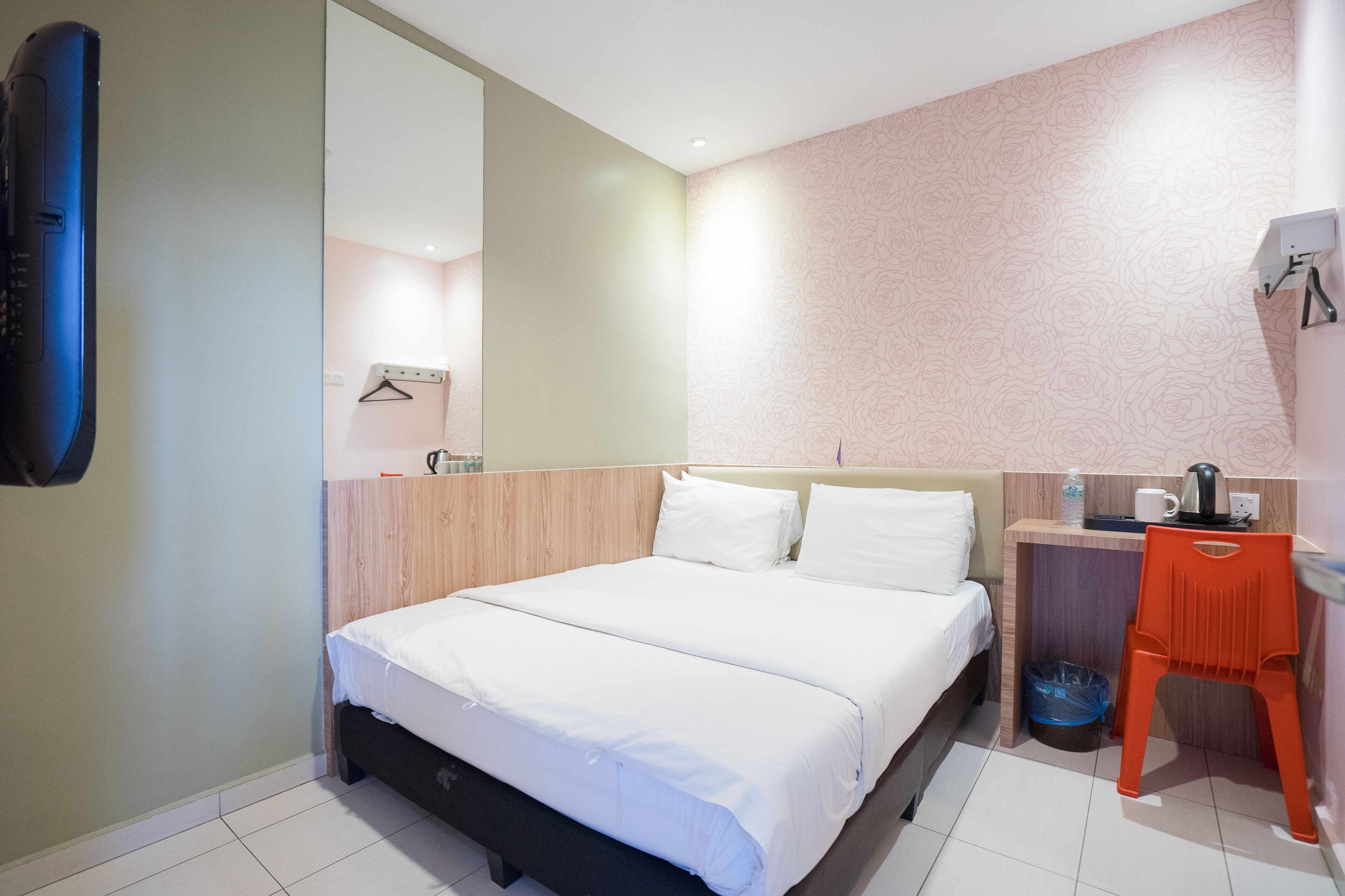 Quarto de hotel com cama, escrivaninha, cadeira, espelho e televisão fixada na parede.