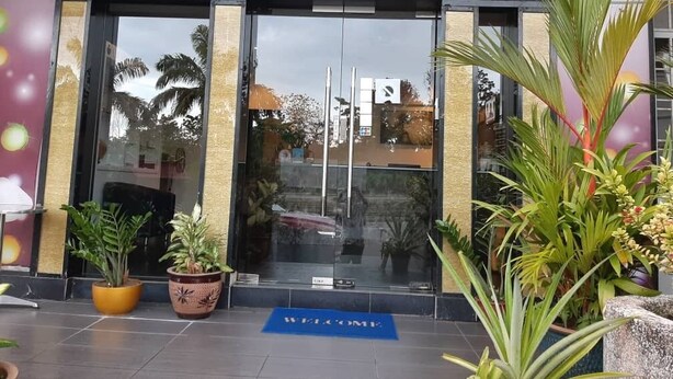 The entrance of Hotel Cappuccino with a clear glass facade, a welcome mat, and potted plants in front.