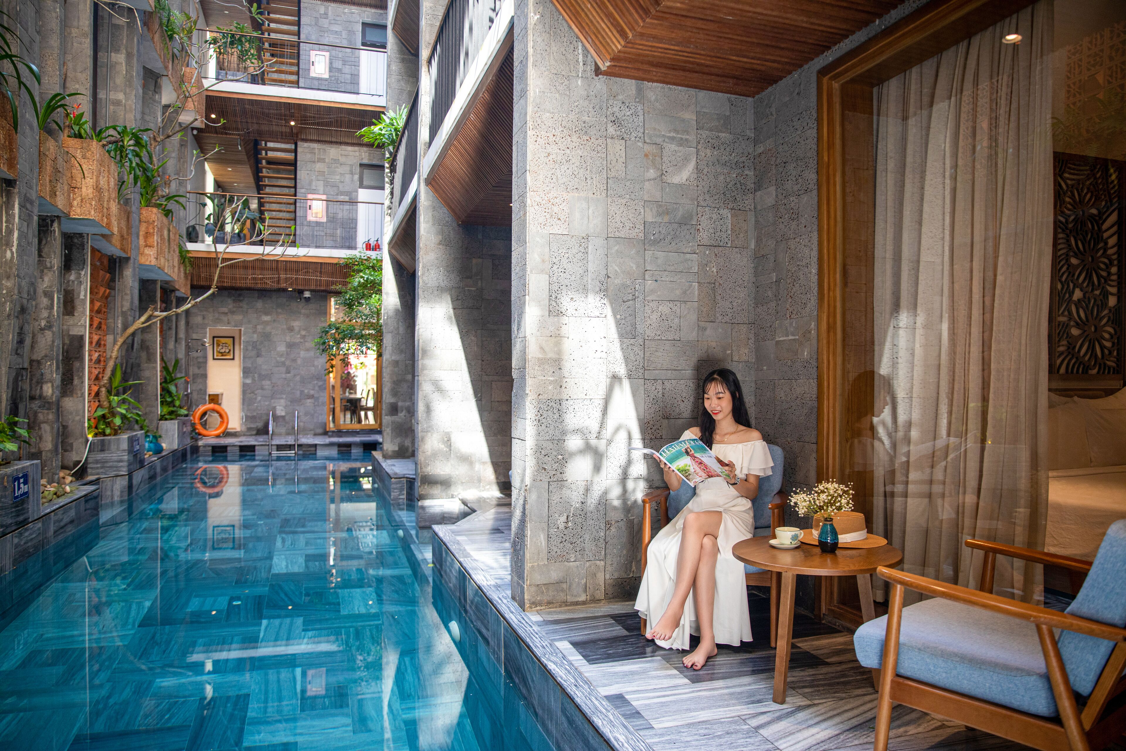 Un espace piscine intérieur moderne, avec un mur en pierre, un plafond en bois et un coin salon comprenant une table et des chaises.