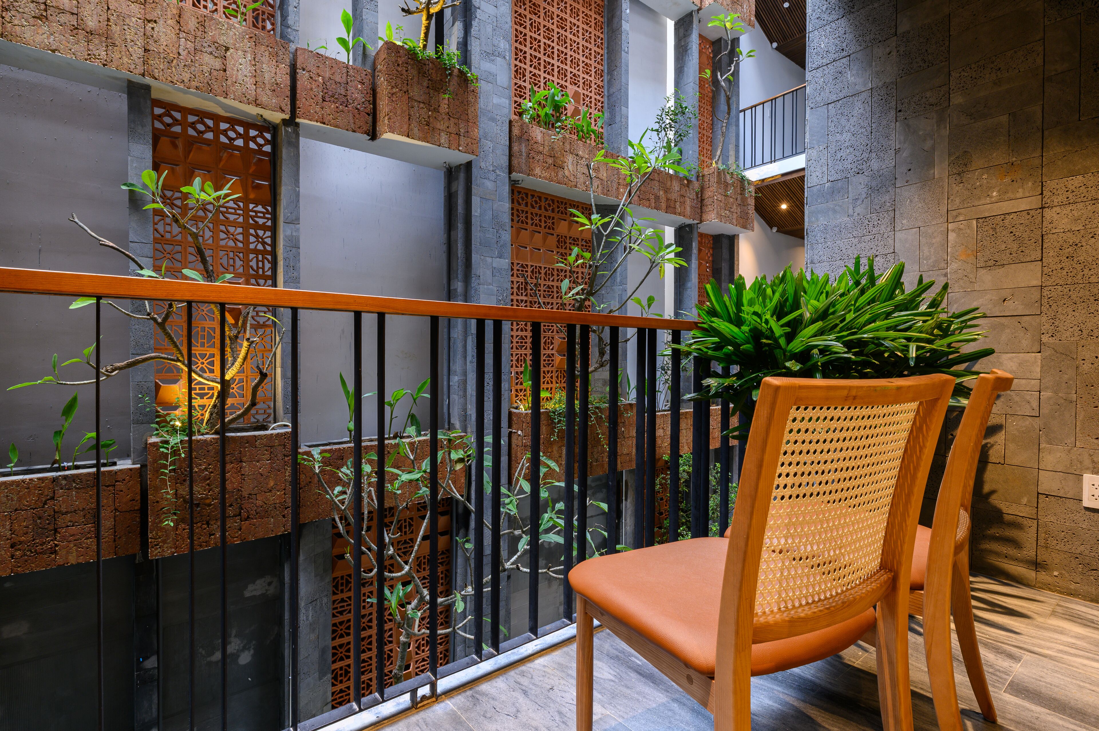 A balcony with a wooden chair, brick walls, and greenery.