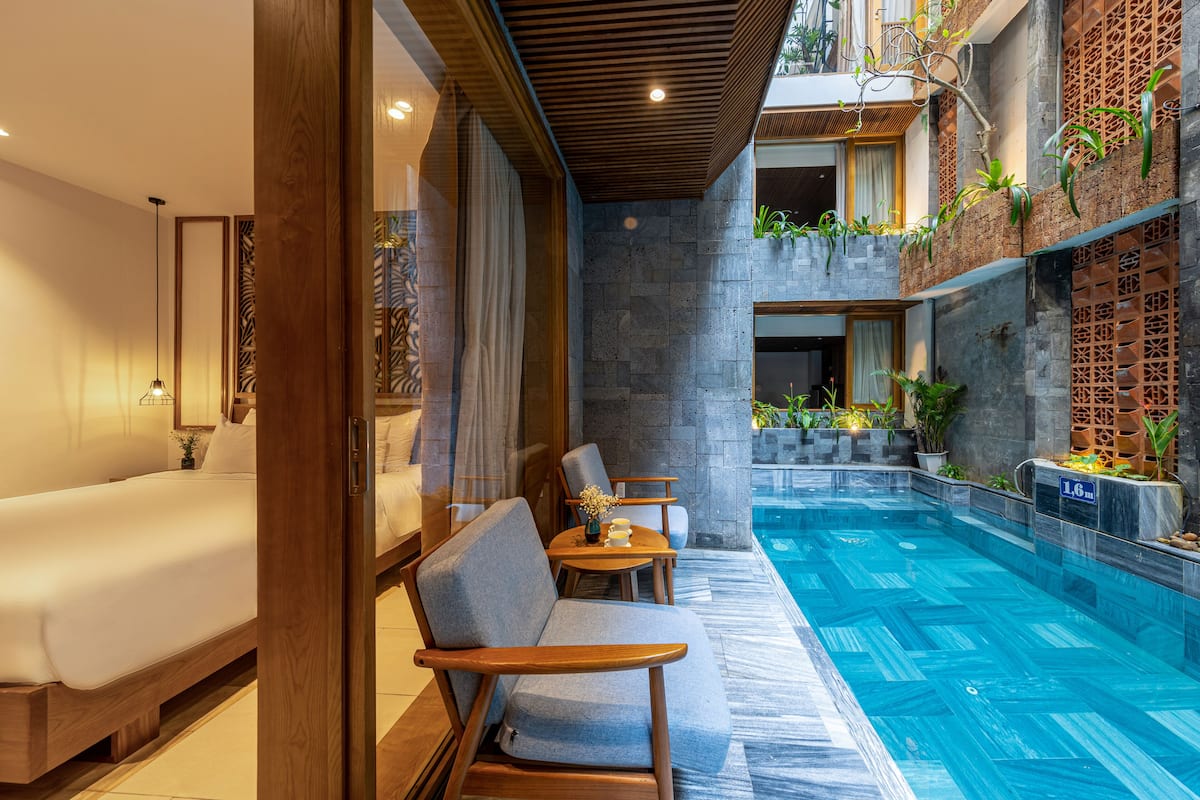 Una habitación de hotel moderna con una cama grande, un espacio de descanso con vista a la piscina y una mesita con un florero.