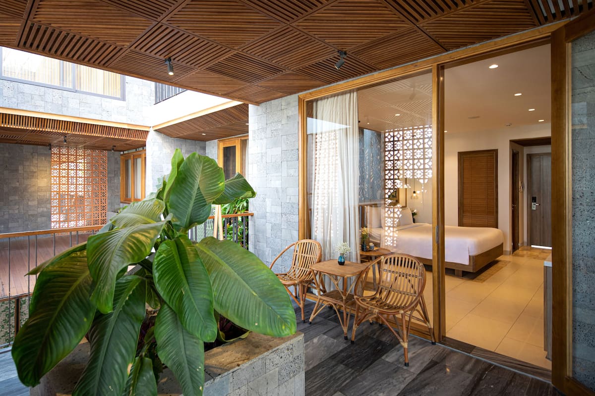 Habitación de hotel moderna con una planta grande en maceta, muebles de madera y vista de la habitación contigua.