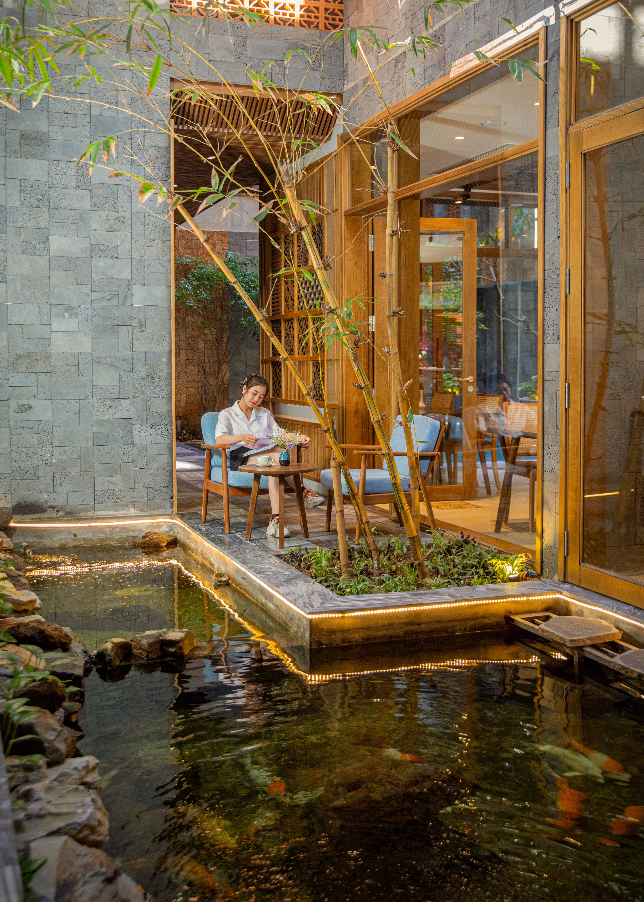 A serene indoor garden with a koi pond, wooden seating, and a glass door leading to a dining area.