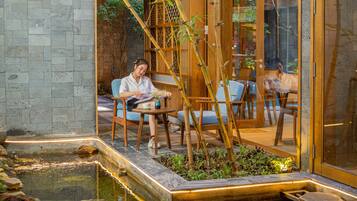A serene indoor garden with a koi pond, wooden seating, and a glass door leading to a dining area.