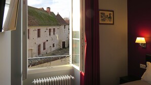 A hotel room with a view of a stone building, a radiator, a bed, and a wall-mounted lamp.