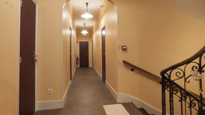A hotel hallway with carpeted floors, a handrail on the right, and a ceiling light fixture.