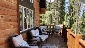 Une terrasse en bois, agrémentée de chaises et d’une table en osier, le tout entouré d’une balustrade en bois.