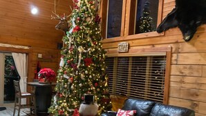 L’intérieur chaleureux d’un chalet, avec un sapin de Noël décoré, un canapé en cuir et une tête d’animal empaillée accrochée au mur.
