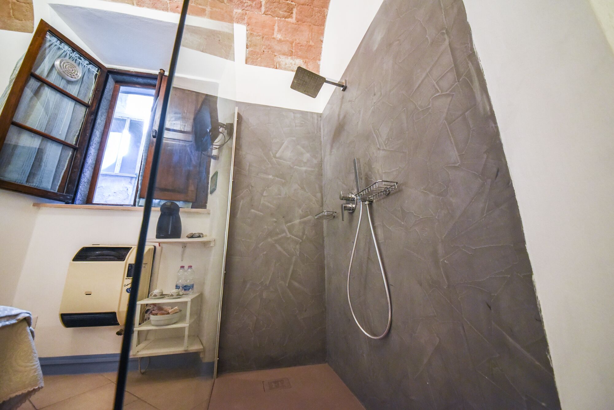 Un baño con ducha, inodoro y lavamanos. Hay una ventana con cortinas y una pared de ladrillo.