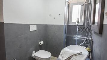 A bathroom with a bidet, toilet, and a shower enclosure.