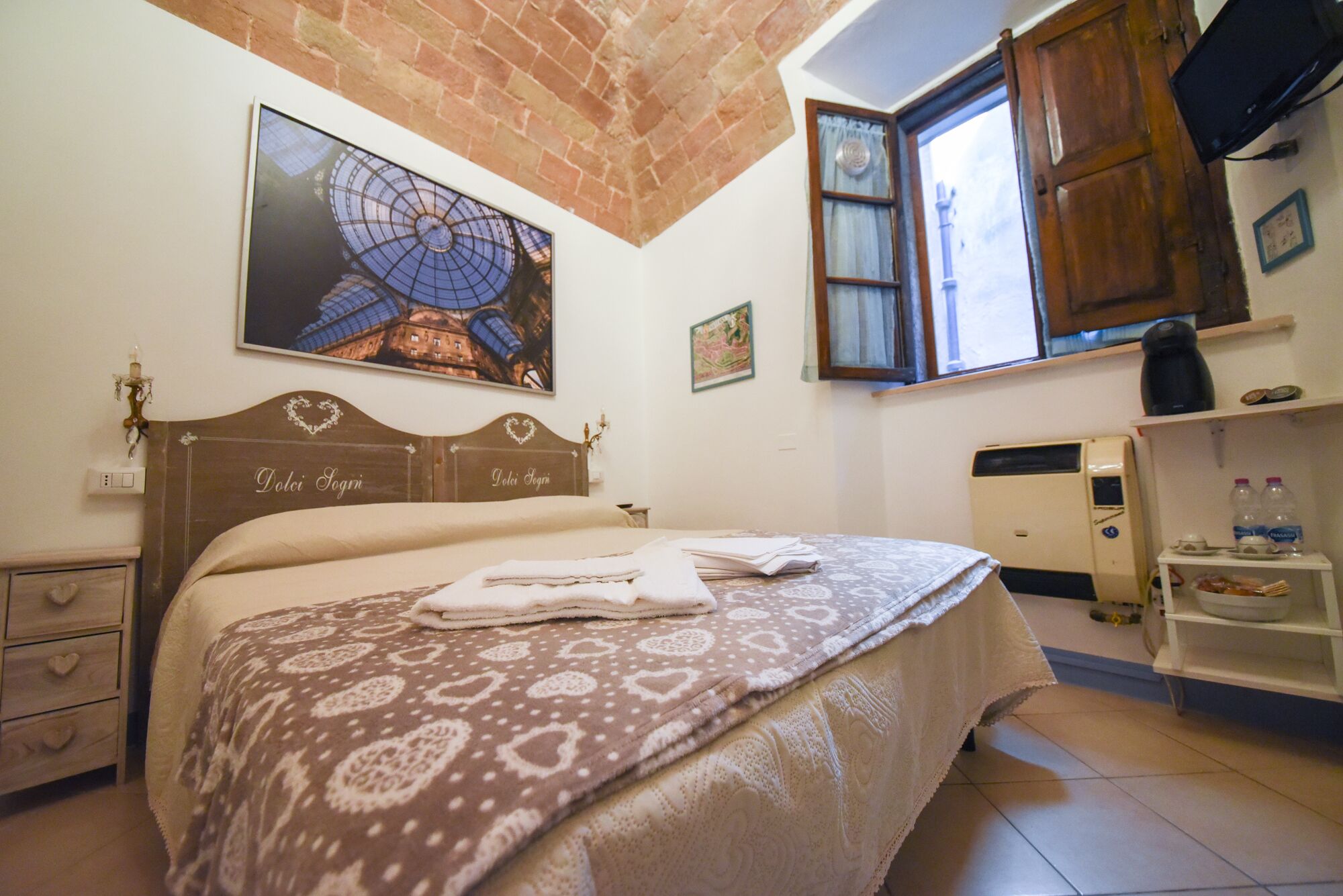 A bedroom with a bed, a nightstand, a wall-mounted TV, a window, and a radiator.