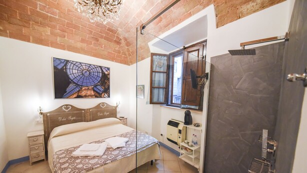 A bedroom with a bed, a nightstand, a dresser, a shower, and a large window.