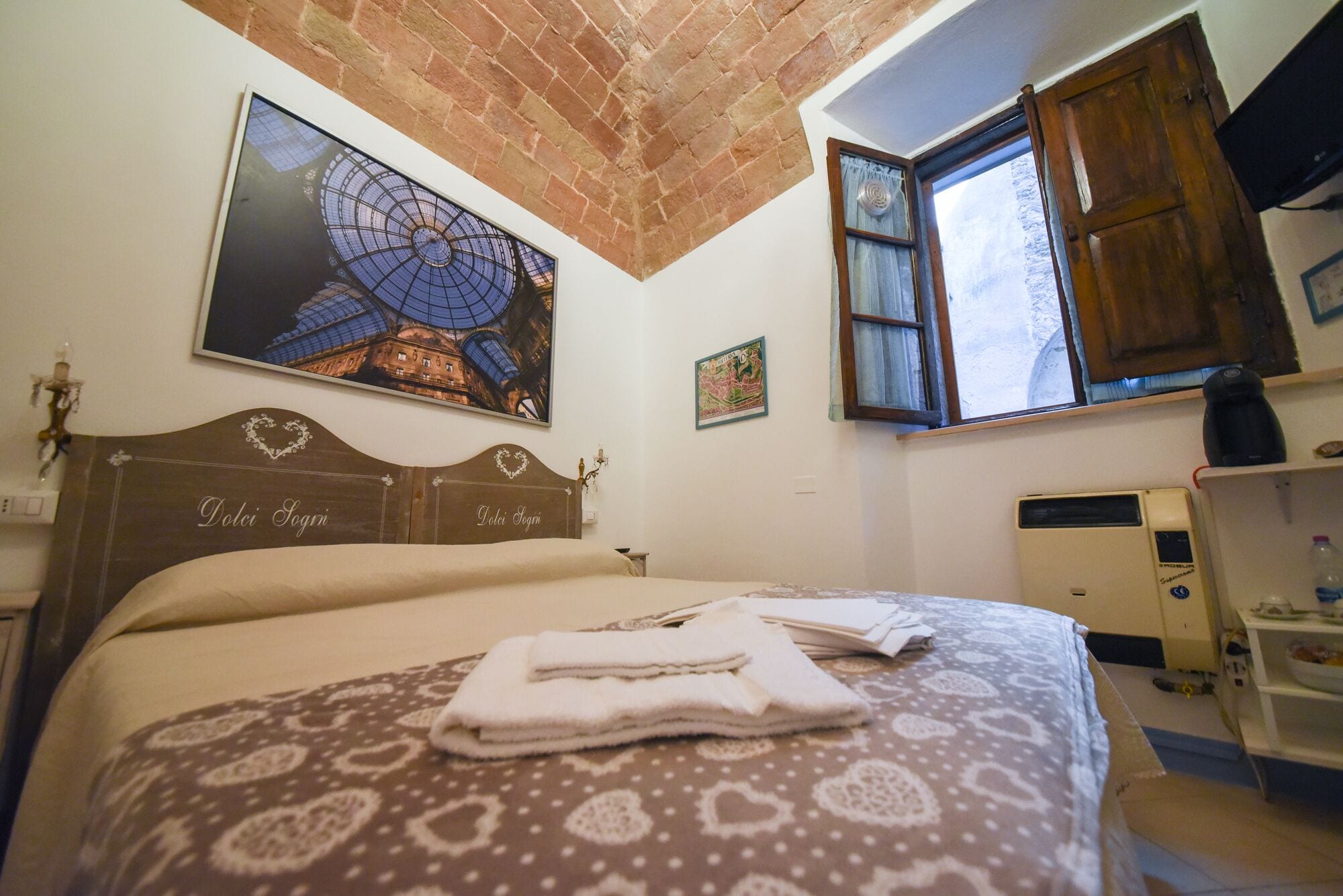 A bedroom with a bed, a radiator, a window, and a wall-mounted TV.