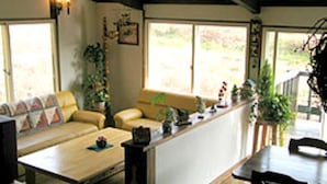 A cozy living area with a sofa, coffee table, and a dining table with chairs. There are potted plants and a window providing natural light. - Pension Marionette (Hokuto)