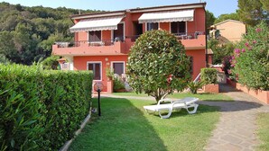A two-story building with balconies, a garden with a bench, and a pathway leading to the entrance. - Apartment in Capoliveri near Sandy Beaches (Capoliveri)