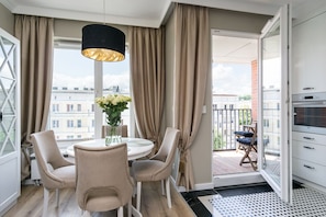 A modern dining area with a round table and four chairs, a pendant light, and a view of the city through large windows.