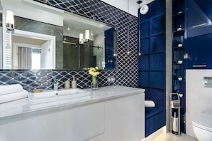 A modern bathroom with a large mirror, a white sink, and a blue accent wall.