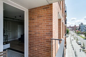 A balcony with a brick wall, a view of a city street, and a door leading to an interior space.