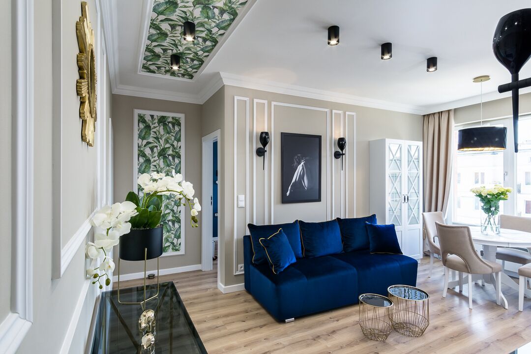A modern living room with a blue sofa, a glass coffee table, and a dining area with a white table and chairs.