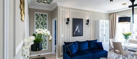 A modern living room with a blue sofa, a glass coffee table, and a dining area with a white table and chairs.
