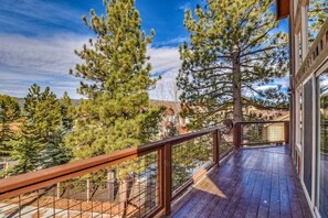 A wooden deck with a metal railing overlooking a forested area. - Goldmine Lakeview by Destination Big Bear : Luxury Lake & Mountain Views with Pool Table & Hot Tub! Walk to Village! (Big Bear Lake)