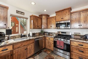 A kitchen with wooden cabinets, stainless steel appliances, and a granite countertop. - Goldmine Lakeview by Destination Big Bear : Luxury Lake & Mountain Views with Pool Table & Hot Tub! Walk to Village! (Big Bear Lake)