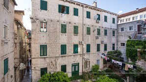A narrow street with buildings featuring stone facades and green shutters. Clothes are hanging on a line outside one building. - JR Luxury Guesthouse (Split)