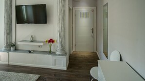 A modern room with a flat-screen TV mounted on the wall, a white console table with a vase of flowers, and a door with a security lock. - JR Luxury Guesthouse (Split)