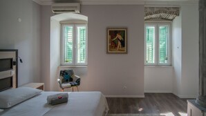 A bedroom with a bed, two windows with shutters, a chair, a painting, and an air conditioning unit. - JR Luxury Guesthouse (Split)