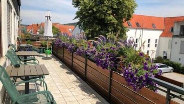 A balcony with a wooden fence, green chairs, and purple flowers. - Gasthof's Gräbele (Tuebingen)