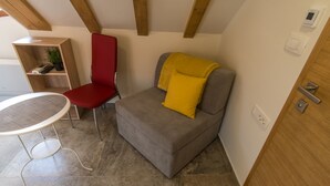 A compact living space with a grey sofa, a red chair, a small table, and a wooden shelf with a plant. - JR Luxury Guesthouse 2 (Split)