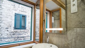 A bathroom with a large window, stone wall, and a wooden-framed mirror. - JR Luxury Guesthouse 2 (Split)