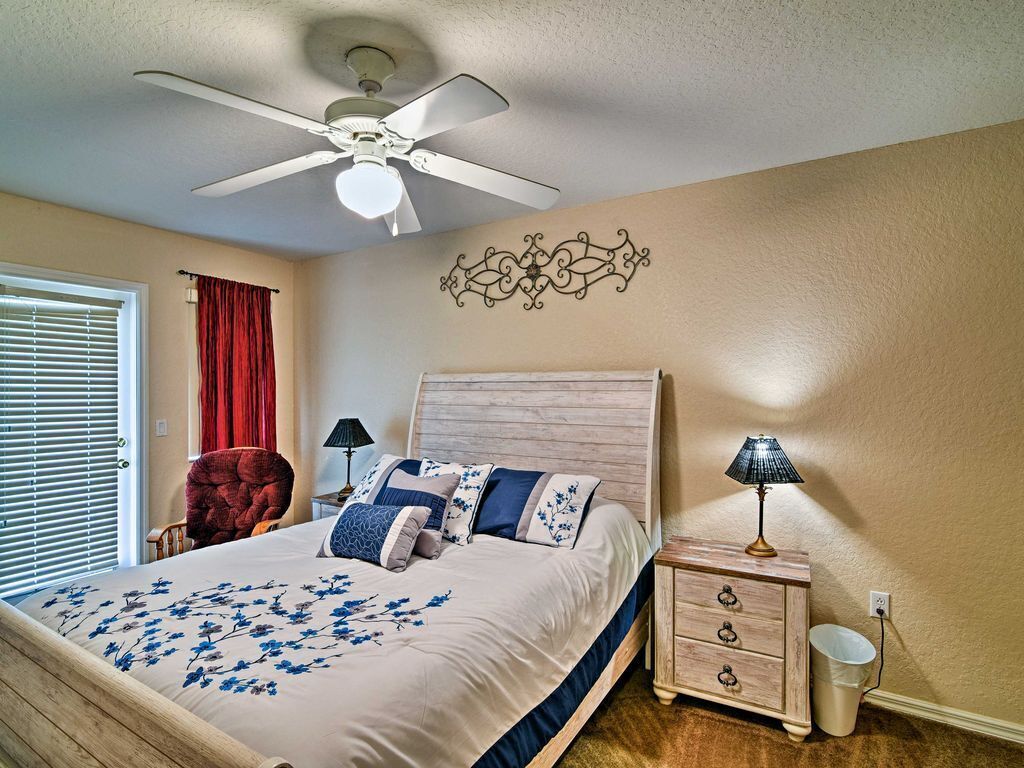 A bedroom with a bed, a ceiling fan, a nightstand, a lamp, a chair, and a decorative wall piece.