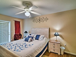 A bedroom with a bed, a ceiling fan, a nightstand, a lamp, a chair, and a decorative wall piece. - Gorgeous 4bd/3ba Reunion Resort Near Disneyland (Kissimmee)